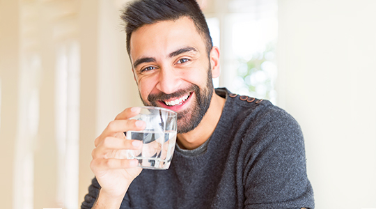 Ein lachender Mann mit einem Glass Wasser in seiner Hand