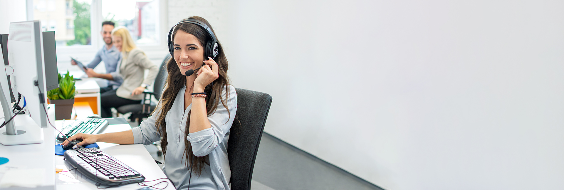 Frau mit Headset sitzt in einem Büro und lächelt in die Kamera