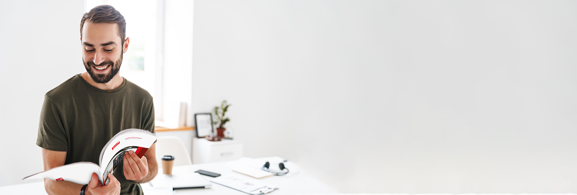 Junger Mann steht in einem Raum und blättert in einem Katalog